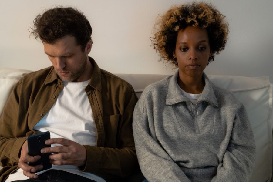 A couple side by side but disconnected, one lost in a phone